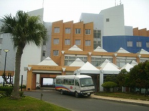 白とオレンジを基調とした近代的な建物の正面に、屋根付きのエントランスと「WELCOME SPACE」と書かれた看板があり、周囲にはヤシの木や低木が植えられたリゾート風の雰囲気を持つおきえらぶフローラルホテルの写真