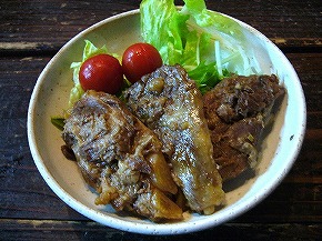 茶色く煮込まれた豚肉料理の「ナンコツ」が3切れあり、横にレタスとミニトマトが添えられた和風の木製テーブル上の写真