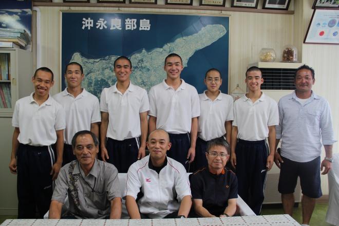 白いポロシャツと紺色のズボンを着た複数の学生が上段と下段に分かれて並び、その両脇に男性が2人立ち笑顔で撮影している写真