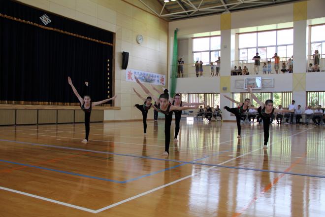 体育館で黒い衣装の生徒たちが一列に広がりバランスを取りながらダンス演技を披露する写真