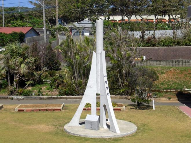 白くて高くそびえる抽象的なデザインの学びの塔が、手入れされた芝生の庭の中心にある円形の台座の上に立っている、白くて高くそびえる抽象的なデザインの学びの塔の写真