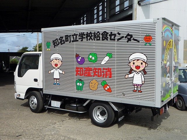 知多町立学校給食センター、知産知消と文字と書かれ、大根、キャベツ、那須など6種類の野菜と給食着の男女のイラストが側面に描かれた白い小型のアルミ製の給食運搬トラックの写真