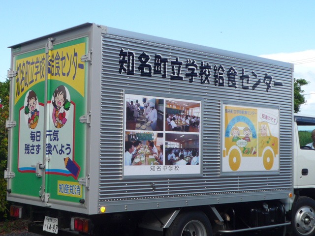 知多町立学校給食センターの文字が上部に書かれ、給食の様子や運搬トラックのイラストなどのパネルが側面に描かれたアルミ製の運搬トラックの写真