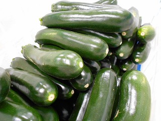 ツヤのある濃い緑色のズッキーニが、山積みになって大量に重ねられている写真