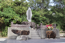 石造りの台座に囲まれた慰霊碑が中央に立ち、碑面には文字が刻まれ、両脇には花が供えられている写真。