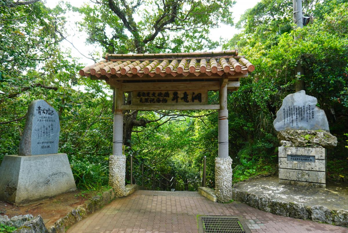 濃い緑の木々に囲まれた場所に、赤茶色の瓦を載せた屋根の門が立っており、門に「昇龍洞」と書かれ、その両脇には石碑が配置されている写真