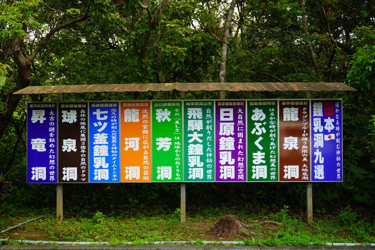 濃い緑の木々を背景に、昇龍洞を含む「日本の鍾乳洞九選」として九つの鍾乳洞の名称とその都道府県、キャッチフレーズがカラフルな看板に印刷されている写真
