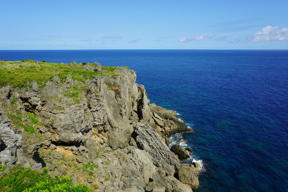 濃い青色の海に面した断崖絶壁が広がり、崖の上は草に覆われ、水平線まで広がる青空と海の田皆岬の写真