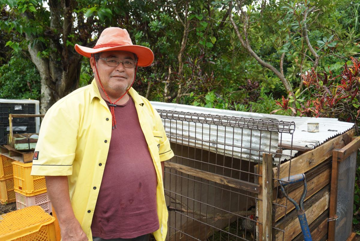 緑豊かな木々や植物を背景にオレンジ色のカウボーイハットをかぶった山下芳也氏の写真