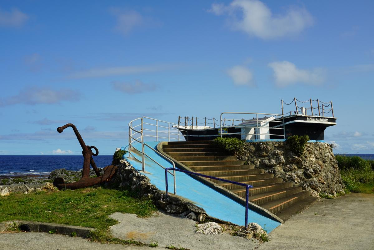 青い手すりと青いスロープを持つ石造りの階段の上に、船の形をしたモニュメントが設置された展望台の写真