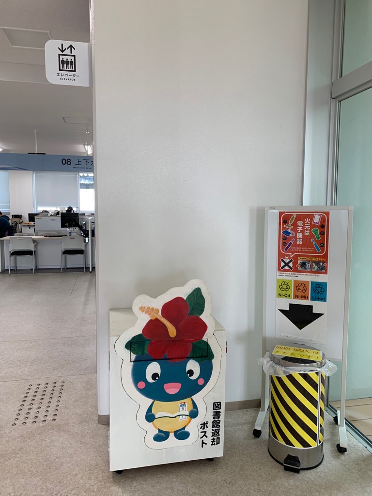 白い壁の前にご当地キャラクター「ちなボー」が描かれた図書館返却ポストの写真