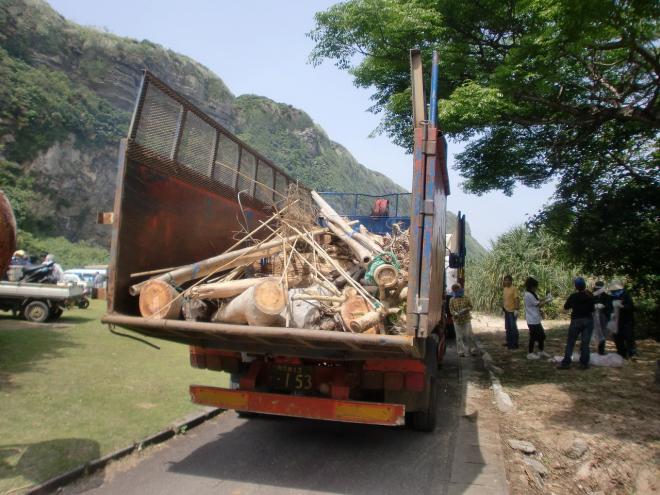 海岸沿いの道路に停車した荷台が大きく開いたダンプに、海岸清掃で集められた流木やごみが山積みになっている写真
