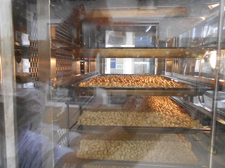 ガラス扉の業務用オーブンの中に、何段ものトレーに敷き詰められた大量の食品が均等に焼かれている様子を扉越しに映した写真