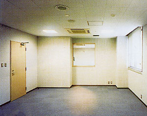 薄いベージュ色の壁と天井、濃い青灰色のカーペットが敷かれた何も置かれてない空間のスタジオ内部の写真