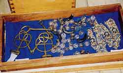 青い布の上に置かれた、金色の金属製の考古学的遺物や、ビーズ、勾玉のような黒い石の装飾品など木製の箱に収められたノロの遺品の写真