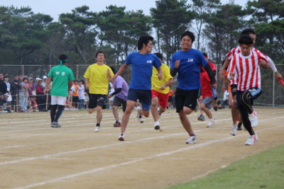 リレー競技で、ユニフォーム姿の選手たちがトラックを力強く走り、バトンの受け渡しを行っている瞬間の写真