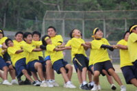 綱引き競技で、黄色のTシャツを着用した多くの選手が綱を握り、顔を上に向けて真剣な表情で力を合わせて引いている綱引きの競技の様子の写真