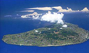 青い海に囲まれた緑豊かな島全体が写っており、島の中央付近に大きな白い雲がかかっている様子を捉えた町全景の航空写真