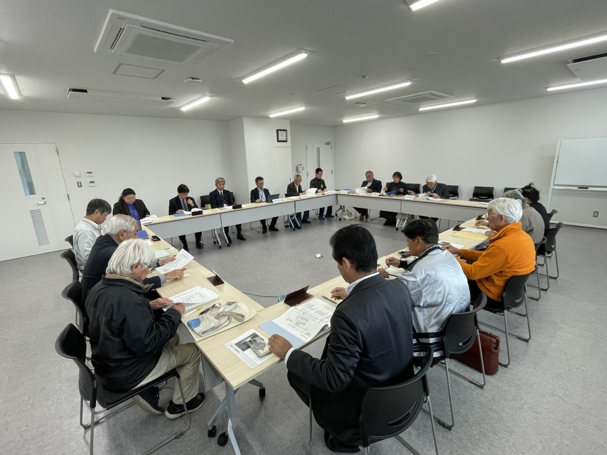 広々とした会議室に、多くの参加者がロの字型に並べたテーブルに着席し、資料を広げて熱心に議論している様子を斜め後方から捉えた編さん委員会の写真