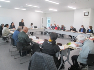 室内で多くの男女がロの字型に並べられたテーブルに座り、数人の参加者が資料にメモを取り、黒い服の男性が立って話している集落・民俗部会の様子の写真