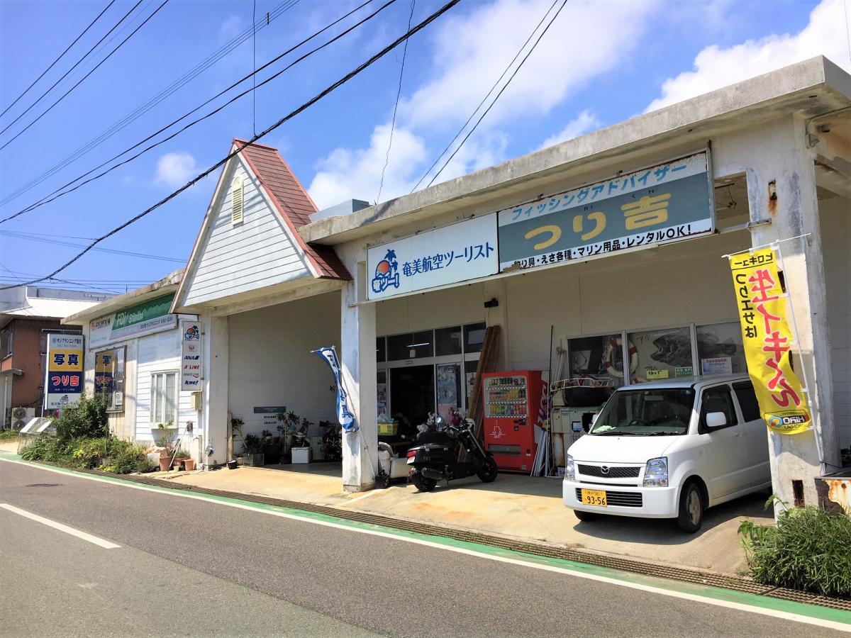 道路沿いにある「奄美航空ツーリスト」と「フィッシングアドバイザーつり吉」の看板を掲げた平屋の店舗の写真