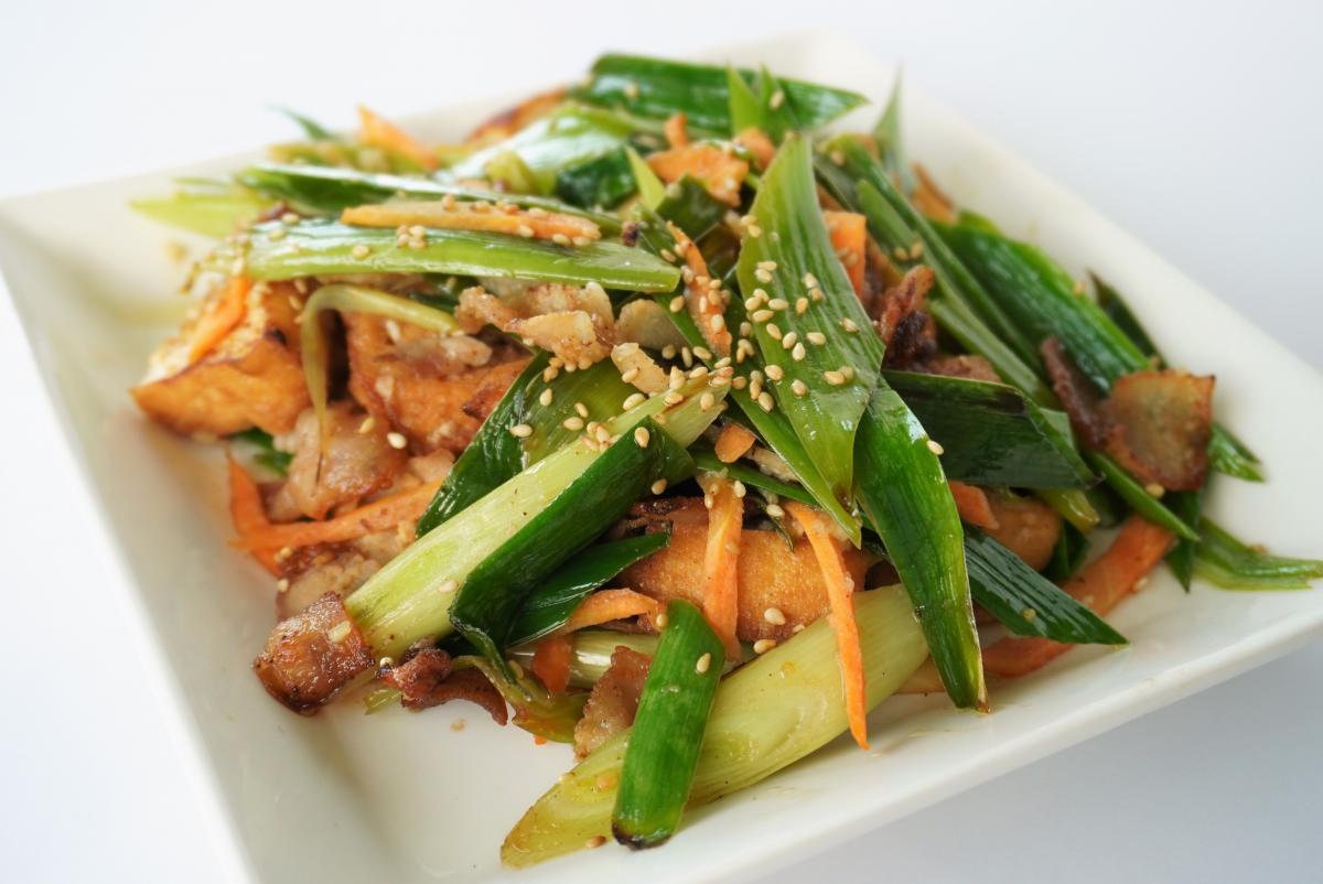 ニンニクの葉と細切りにんじんを中心に、豚肉と厚揚げを炒めて白ごまを散らした料理の写真