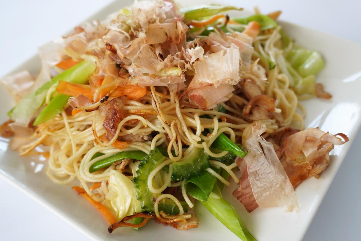 細切りのゴーヤやにんじん、キャベツと麺を炒め、上にかつお節をたっぷり載せたソーメンチャンプルーの写真