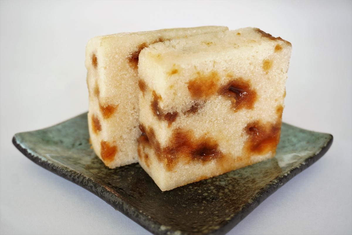 茶色の黒糖が散りばめられた白い二切れの蒸し菓子が、黒と緑の釉薬のかかった四角い陶器の小皿に斜めに置かれた写真