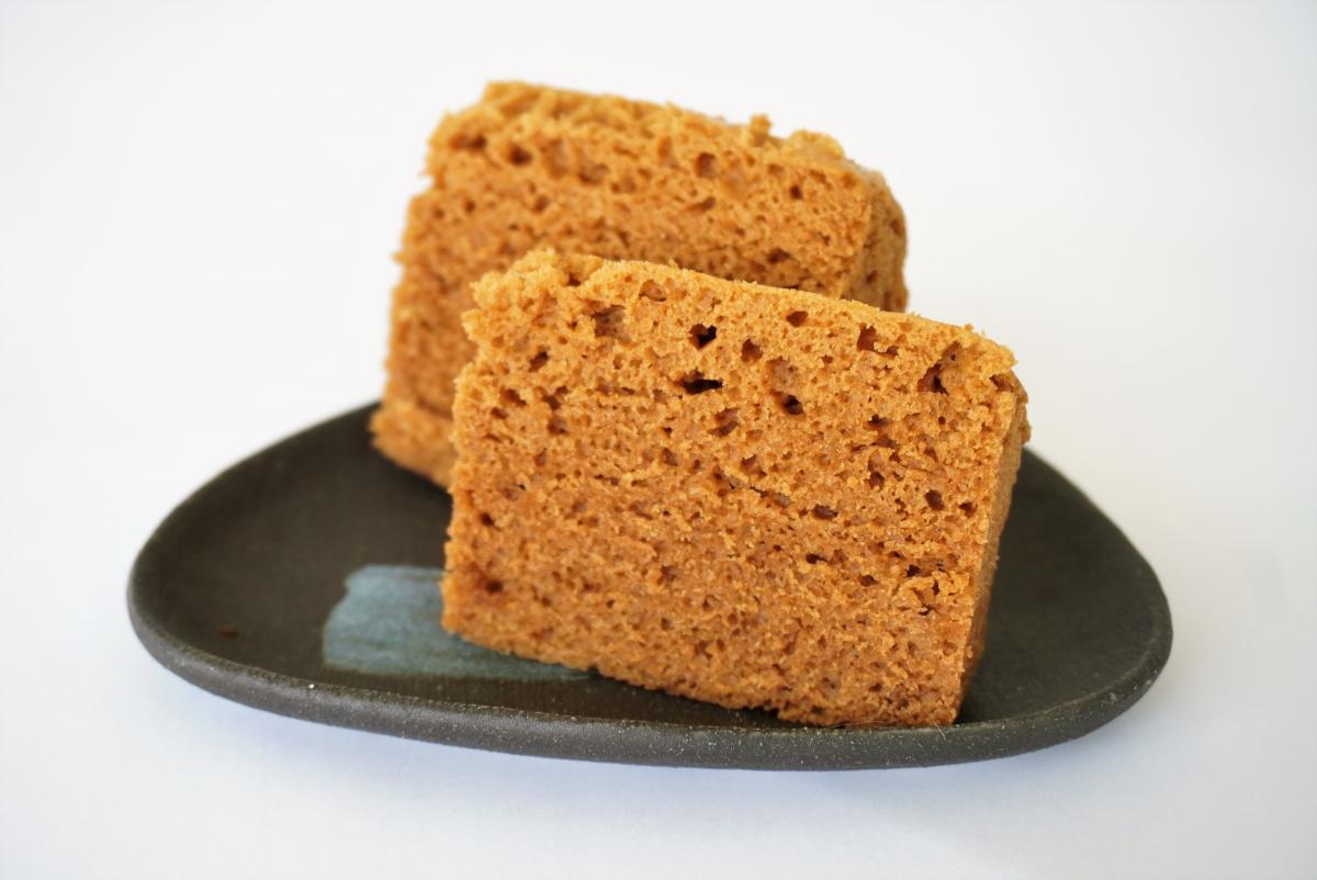 茶色くきめ細かな、黒糖を使用したような蒸し菓子の切り身が二つ、黒い釉薬のかかった陶器皿に盛られている写真