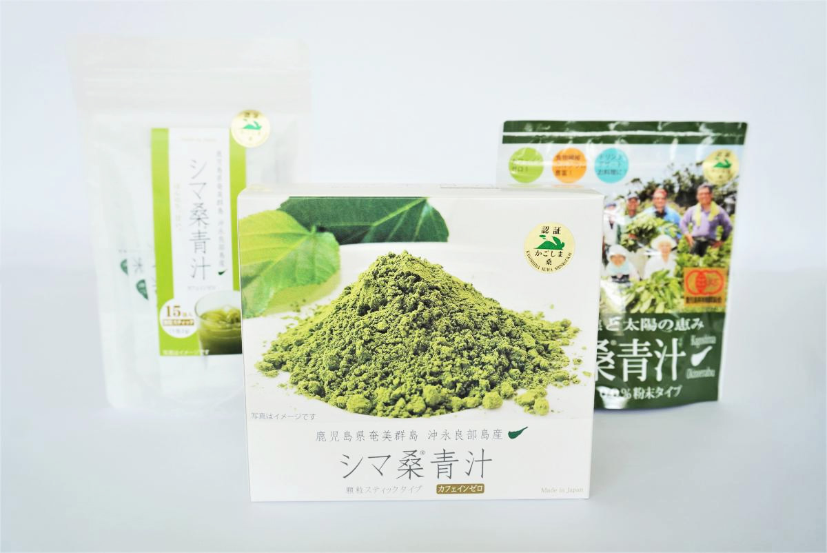 手前に緑色のパッケージの「シマ桑青汁」の箱と奥に白いパッケージの袋と右奥に別の袋の青汁製品が並べられ、中央の箱には鮮やかな緑の粉末が山盛りに印刷された商品の写真