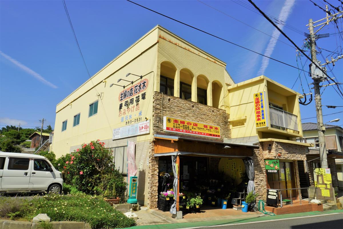 薄い黄色の壁とレンガ調の石材で装飾された二階建ての建物の、一階部分が花屋と店舗になっている主婦の店 花水木の写真