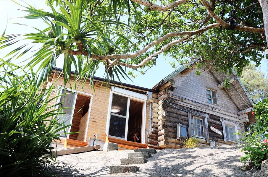 丸太を組んだログハウス風の建物で、亜熱帯の植物に囲まれた上り坂の上に立つコテージ ビーバー海の外観写真