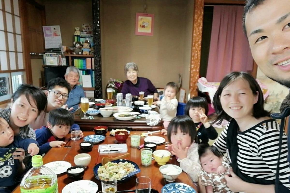 和室の座敷に勘里さん一家と複数の方々が集まり、木製の座卓に和食の料理や飲み物が並べられいる写真