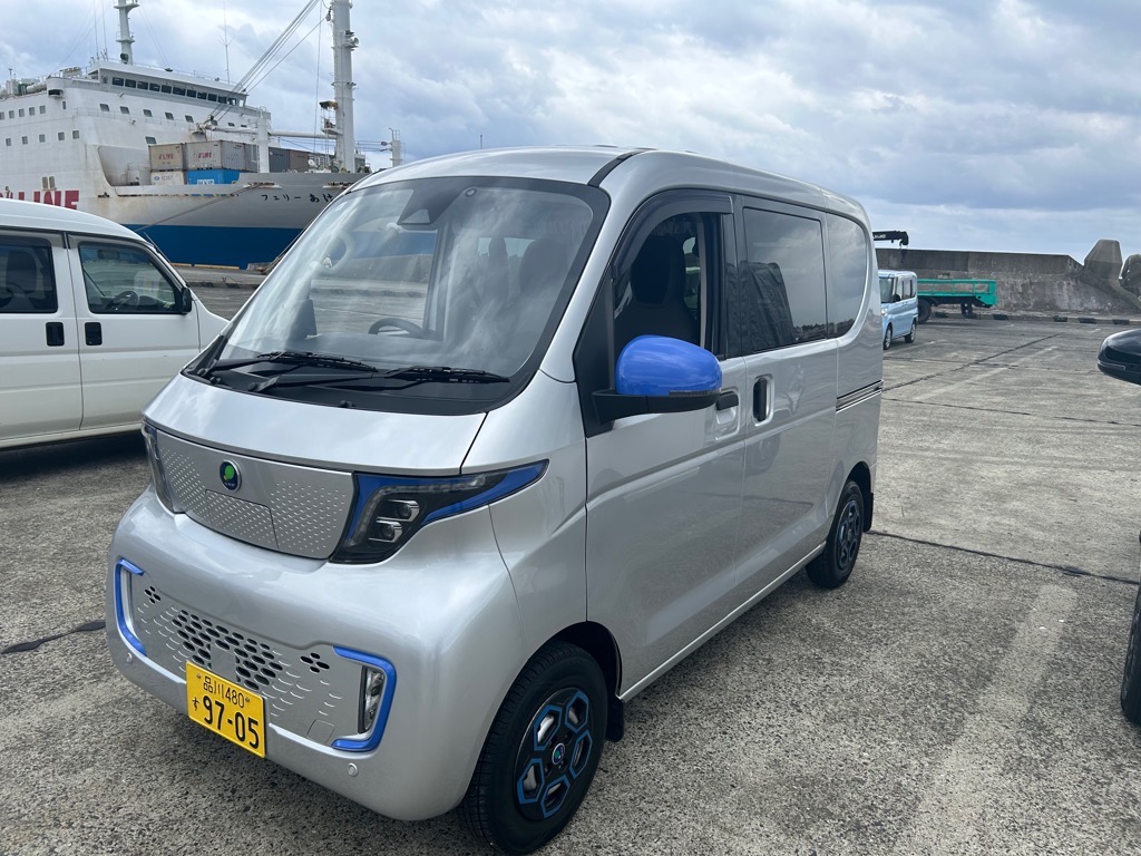 港の駐車場に停められたシルバーと青いサイドミラーとアクセントが特徴的なデザインの電気自動車の写真