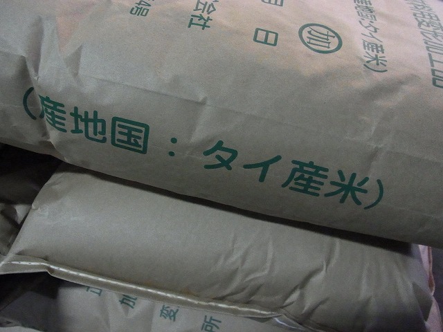 濃い茶色の紙袋に緑色の太字で「産地国：タイ産米」と印字された米袋が積み重ねて置かれている写真