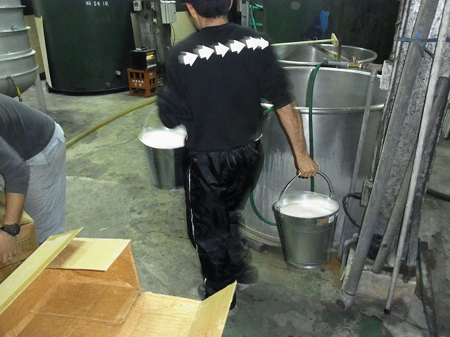 男性が、両手に銀色のバケツを一つずつ持ちドラムに運搬する様子の写真